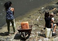 大規模停電に見舞われたベネズエラの首都カラカスで、破裂した水道管から下水用水路に流れ込む水をくもうとする女性と赤ちゃんを抱いた少女（2019年3月11日撮影）。(c)JUAN BARRETO / AFP