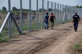 ハンガリーとセルビアの国境に設置されたフェンスと、そばを歩く移民ら（2015年8月27日撮影）。(c)AFP/ATTILA KISBENEDEK