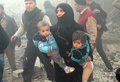 空爆を受けたシリア北部アレッポ（Aleppo）の反体制派が掌握する地区で、子どもを抱えて歩く女性（2013年12月15日撮影）。(c)AFP/MOHAMMED AL-KHATIEB