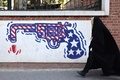 イラン・テヘランで、旧米国大使館の外壁に描かれた星条旗模様の銃の絵の横を歩く女性（2024年11月6日撮影）。(c)ATTA KENARE / AFP