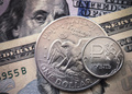 ロシアの首都モスクワで撮影されたロシアの通貨ルーブル硬貨（右）と1米ドル硬貨。背景は米ドル紙幣（2022年3月15日撮影、資料写真）。(c)AFP