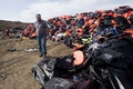 ギリシャのレスボス島モリボスに山積する難民が捨てた救命胴衣などのごみと、そのそばに立つ市職員（2015年9月26日撮影）。(c)AFP/IAKOVOS HATZISTAVROU