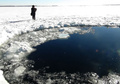 ロシア・チェリャビンスク（Chelyabinsk）州のチェバルクリ湖（Lake Chebarkul）で、表面の氷に開いた直径6メートルほどの穴のそばに立つ警察官（2013年2月15日撮影）。(c)AFP/CHELYABINSK REGION POLICE DEPARTMENT