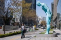 韓国ソウルで、彫刻家のユ・ヨンホさんの作品「グリーティング・マン」の前を電動スクーターで通り過ぎる男性（2022年4月8日撮影）。(c)Anthony WALLACE / AFP
