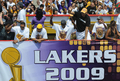 08-09NBAファイナルを制したロサンゼルス・レイカーズ（%%Los Angeles Lakers%%）の優勝パレードが17日、ロサンゼルス（Los Angeles）で行われ、数万人ものバスケットボールファンが祝福のため、市内中心部に詰めかけた。レイカーズの本拠地ステープルズ・センター（Staples Center）から始まったパレードは、8万人のファンが待つロサンゼルス・メモリアル・コロシアム（Los Angeles Memorial Coliseum）まで行われ、数百人の警察官が動員され。写真はバスからファンの声援に応えるレイカーズの選手たち。（2009年6月17日撮影）(c)AFP/ROBYN BECK