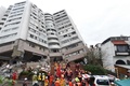台湾東部・花蓮で、地震により大きく傾いた建物から不明者の遺体を収容する救助隊（2018年2月8日撮影）。(c)AFP PHOTO / Anthony WALLACE