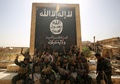 イラク・ハウィジャに進攻した際、ISの旗を描いた壁画の前で写真撮影に臨む、政府軍のIS掃討作戦に参加する民兵組織「人民動員隊」の隊員ら（2017年10月5日撮影）。(c)AFP/AHMAD AL-RUBAYE