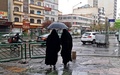 イランの首都テヘランで、傘を持って歩く女性2人（2022年12月5日撮影）。(c)ATTA KENARE / AFP