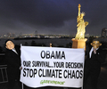 写真は、都内でレインボーブリッジ（Rainbow Bridge）と自由の女神像を背に、バラク・オバマ（Barack Obama）米大統領と鳩山由紀夫（Yukio Hatoyama）首相のマスク姿で「オバマ（大統領）、われわれの生存はあなたの決定にかかっている。気候の混乱を止めて」と書かれた横断幕を掲げ、気候変動問題への取り組みを訴えるグリーンピースの活動家（2009年11月13日撮影）。(c)AFP/Kazuhiro NOGI
