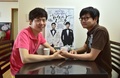 韓国ソウルの自宅で、自分たちの結婚式のポスター（中央奥）と共に写真撮影に応じる金趙光秀さん（右）と金承煥さんのカップル（2015年7月15日撮影）。(c)AFP/JUNG YEON-JE