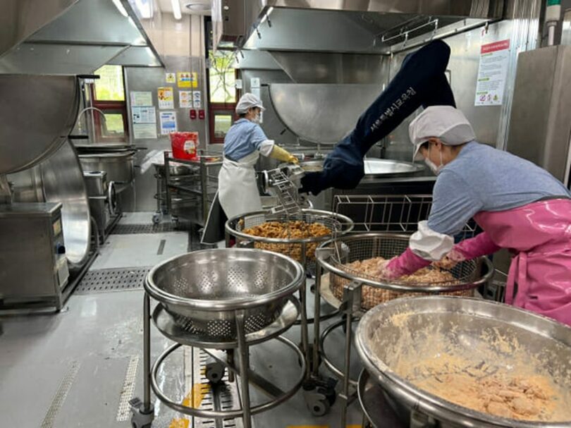 ソウルのある中学校の給食室の全景。現場の調理師らが調理ロボットと共に料理をしている(c)KOREA WAVE