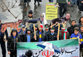 イランの首都テヘランで行われたイラン革命40周年記念式典で、顔を国旗の色に塗って行進する子どもたち。手に持っているのは、犬の胴体の写真に（左から）ドナルド・トランプ米大統領、サウジアラビアのサルマン国王、イスラエルのベンヤミン・ネタニヤフ首相の顔写真が貼られたプラカード（2019年2月11日撮影）。(c)ATTA KENARE / AFP