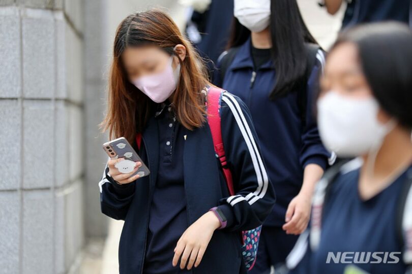 ソウル市内の中学校前で、スマートフォンを見ながら下校する生徒たち(c)NEWSIS