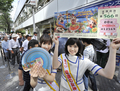 サマージャンボ宝くじをアピールするキャンペーンガールと、都内の宝くじ売り場に並んだ人々（2009年7月13日撮影）。(c)AFP/Yoshikazu TSUNO