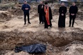 ウクライナの首都キーウ近郊ブチャの教会の集団埋葬地で、祈りをささげる神父（2022年4月7日撮影）。(c)RONALDO SCHEMIDT / AFP