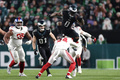 23NFL第16週、フィラデルフィア・イーグルス対ニューヨーク・ジャイアンツ。ニューヨーク・ジャイアンツのデイン・ベルトン（中央下）を跳び越えるフィラデルフィア・イーグルスのディアンドレ・スウィフト（2023年12月25日撮影）。(c)Adam Hunger/Getty Images/AFP