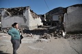 ギリシャ中部テッサリア地域のダマシ村で、地震により損壊した建物のそばに立つ女性（2021年3月3日撮影）。(c)Sakis MITROLIDIS / AFP