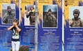 屋外に展示されたウクライナの軍事組織「アゾフ旅団」の戦没者の写真を見て顔を覆う男の子。ウクライナ・キーウで（2024年9月23日撮影）。(c)Sergei SUPINSKY / AFP