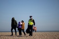 英イングランド南東部ダンジネスに到着した移民と、移民の荷物を運ぶ警官（2022年3月15日撮影）。(c)Ben Stansall / AFP
