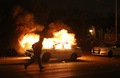 米ミズーリ（Missouri）州ファーガソン（Ferguson）で、黒人青年の射殺事件に抗議するデモが行われる中、燃える警察車両のわきを走り去る警察官（2014年11月24日撮影）。(c)AFP/Getty Images/Justin Sullivan