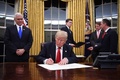 米首都ワシントンのホワイトハウスで、マイク・ペンス副大統領（左）に見守られながら大統領令に署名するドナルド・トランプ大統領（2017年1月20日撮影）。(c)AFP/JIM WATSON