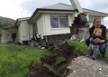 ニュージーランド南島東岸にあるカイコウラで、地震で損壊した家の前に座る母子（2016年11月14日撮影）。(c)AFP/RADIO NEW ZEALAND/ALEX PERROTTET
