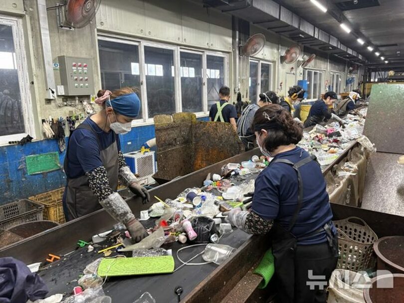韓国・京畿道の資源循環センターで、ベルトコンベヤーを流れるペットボトルや使い捨て容器などを分別する作業員＝7日(c)NEWSIS