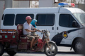中国新疆ウイグル自治区ホータンで、警察車両の脇をバイクで走るイスラム教徒の人たち（2017年6月23日撮影）。(c)Johannes EISELE / AFP