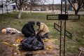 ウクライナ・キーウ近郊のホストーメリで、掘り出されたユーリー・プリリプコ町長の遺体を袋に入れる自治体職員（2022年4月12日撮影）。(c)FADEL SENNA / AFP