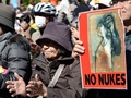 都内の脱原発集会でポスターを掲げる参加者と、その傍らで手をたたく参加者（2014年3月15日撮影）。(c)AFP/TOSHIFUMI KITAMURA