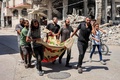 パレスチナ自治区ガザ地区のガザ市東部トゥファ地区で、イスラエル軍の攻撃で犠牲になった人の遺体を毛布で運ぶ住民（2024年7月8日撮影）。(c)Omar AL-QATTAA / AFP