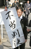 写真は東京高裁前で13日、「不当判決」の幕を掲げ、判決について会見する原告団側弁護人の藤沢整弁護士。(c)AFP/Kazuhiro NOGI