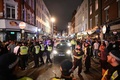 英ロンドンのソーホー地区で、車が通れるようバーの外で飲み騒ぐ人々を誘導する警官（2020年7月4日撮影）。(c)JUSTIN TALLIS / AFP