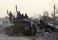シリア首都ダマスカス近郊東グータに入り、装甲兵員輸送車の上に立ち武器を掲げる政府軍（2018年3月4日撮影）。(c)AFP