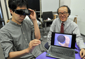 都内の研究室で、ビスケットを実際よりも大きく見せるゴーグルについて説明する東京大学（University of Tokyo）の廣瀬通孝（Michitaka Hirose）教授（右、2012年6月2日撮影）。(c)AFP/Yoshikazu TSUNO