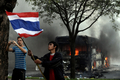タイの首都バンコク（Bangkok）で、タイ軍とタクシン・シナワット（Thaksin Shinawatra）元首相派のデモ隊の衝突中にデモ隊が炎上させたバスとそれを撮影する外国人（左）、デモの参加者（2009年4月13日撮影）。(c)AFP/NICOLAS ASFOURI
