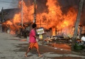 イスラム武装勢力の襲撃を受けたフィリピン南部ミンダナオ（Mindanao）島の商業都市サンボアンガ（Zamboanga）では、12日も治安当局と和平協議に応じないイスラム反政府勢力との戦いが2か所の戦線で続いている。同国政府は、炎に包まれた複数の地区を奪還した。

サンボアンガでは、4日間にわたる戦闘で数千人が避難を強いられている。フィリピン軍報道官によると、同市のサンタカタリナ（Santa Catalina）地区では、治安部隊が進軍する中、家々が炎に包まれた。

警察の支援を受けた少なくとも1500人の兵士が、サンボアンガ郊外のイスラム教徒が多く住む6地区を包囲。これらの地域では、反政府勢力「モロ民族解放戦線（MNLF）」のメンバー約180人が、9日に攻撃を開始して以降潜伏を続けている。反政府勢力は数十人の人々を「人間の盾」にしているため、市民が負傷することを避けたい治安部隊との間でこう着状態が続いている。

写真はサンボアンガで火に包まれる家々の横を通り過ぎる地元住民（2013年9月12日撮影）。(c)AFP/TED ALJIBE