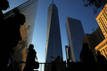 米ニューヨーク（New York）の超高層ビル「ワン・ワールド・トレード・センター（One World Trade Center）」の側面に清掃用の足場が宙づりとなる中、近くを歩く人々（2014年11月12日撮影）。(c)AFP/Getty Images/Spencer Platt