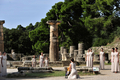 カナダで開催される%%バンクーバー冬季五輪%%の聖火が22日、古代五輪発祥の地、ギリシャのオリンピア（%%Olympia%%）で採火され、バンクーバーまで4万7000キロ以上におよぶリレーをつなぐ最初の走者に渡された。写真はオリンピアにあるヘラ（Hera）神殿前で行われたバンクーバー五輪の採火式で、日光から採火する巫女（みこ）役のギリシャ人女優、マリア・ナフプリオトゥ（Maria Nafpliotou）さん（中央、2009年10月22日撮影）。(c)AFP/ARIS MESSINIS