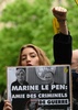 フランスの極右政党「国民連合（RN）」のマリーヌ・ルペン党首が記者会見した会場の外で、ルペン氏とロシアのウラジーミル・プーチン大統領が握手する写真に「マリーヌ・ルペン：戦争犯罪人の友達」と書かれたプラカードを持って抗議するデモ参加者（2022年4月13日撮影）。(c)EMMANUEL DUNAND / AFP