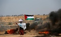 パレスチナ自治区ガザ地区のイスラエルとの境界付近で行われたデモで、頭に袋を乗せ、パレスチナ旗を掲げて炎上するタイヤのそばに立つ女性（2018年6月8日撮影）。(c)AFP PHOTO / SAID KHATIB
