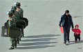 中国四川（Sichuan）省甘孜（Ganzi）チベット族自治州の中心地、康定（Kangding）県を警備する機動隊の背後を歩く市民（2008年3月20日撮影）。(c)AFP/TEH ENG KOON