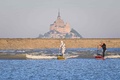 フランス北西部モンサンミシェル湾で、潮汐の波に乗るパドルボードのサーファーたち。中には米SF映画「スター・ウォーズ」シリーズに登場する「ストームトルーパー」の仮装姿も（2025年4月29日撮影）。(c)LOU BENOIST / AFP
