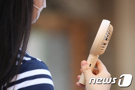 携帯用ミニ扇風機で暑さをしのぐ市民(c)news1