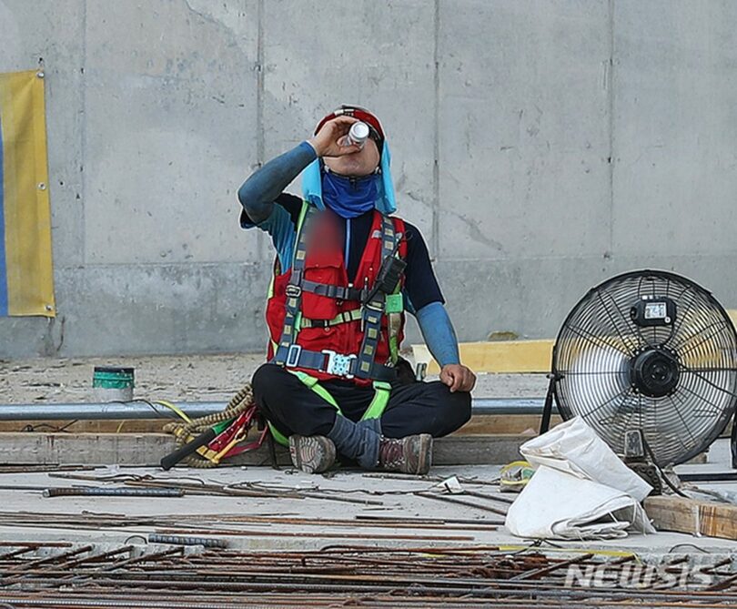 猛暑が続いた2021年7月26日、ソウル市永登浦区の建設現場で日陰に入り休憩する作業員(c)NEWSIS