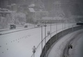 スペイン・マドリード市内の環状道路で作業する除雪車と、道路に並行する道を歩く人々（2021年1月9日撮影）。(c)PIERRE-PHILIPPE MARCOU / AFP