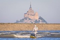 フランス北西部モンサンミシェル湾で、米SF映画「スター・ウォーズ」シリーズに登場する「ストームトルーパー」の仮装で潮汐の波に乗るパドルボードのサーファー（2025年4月29日撮影）。(c)LOU BENOIST / AFP