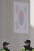 過去5年で最悪規模の黄砂に見舞われた韓国・ソウルで、国旗が掲げられた建物の前で顔を見合わせる、マスク姿の警察官たち（2015年2月23日撮影）。(c)AFP/Ed Jones