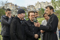 ウクライナの首都キーウ近郊ブチャで集団埋葬地を訪れたロックバンド「U2」のボノさん（中央）とジ・エッジさん（前方左）に自分の携帯電話の画面を見せる教会の神父（2022年5月8日撮影）。(c)Genya SAVILOV / AFP