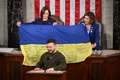 米連邦議会で演説するウクライナのウォロディミル・ゼレンスキー大統領（手前）と、ゼレンスキー氏から贈られたウクライナ国旗を広げるカマラ・ハリス米副大統領（後列左）、ナンシー・ペロシ下院議長（2022年12月21日撮影）。(c)Mandel NGAN / AFP